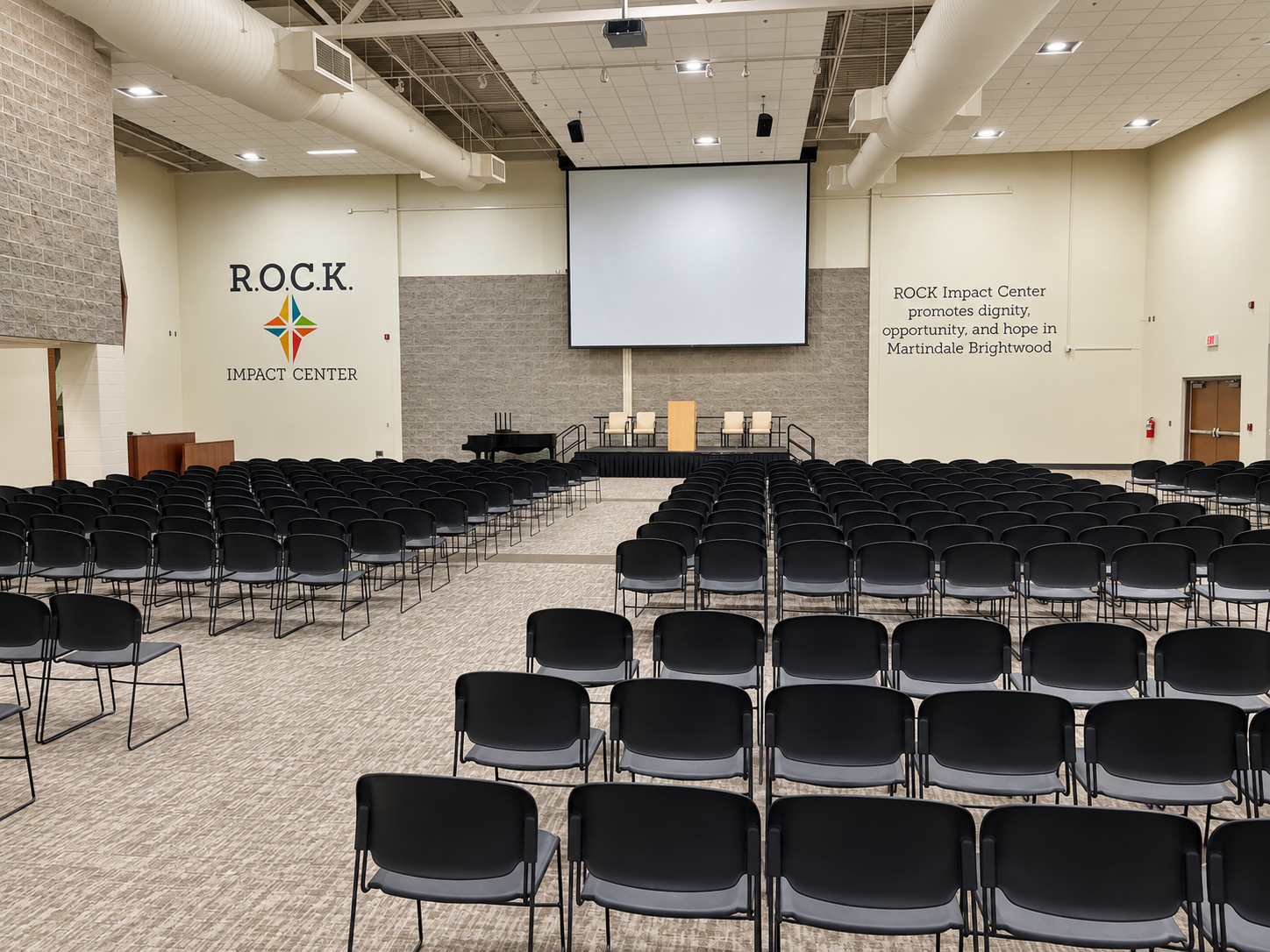 The Cornerstone Auditorium set for an event — long and round tables, rows of chairs, and a stage with a projection screen